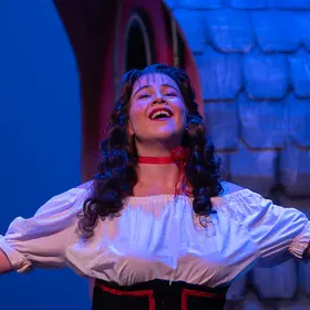 Singer in a white blouse with arms raised, framed by a red stage curtain